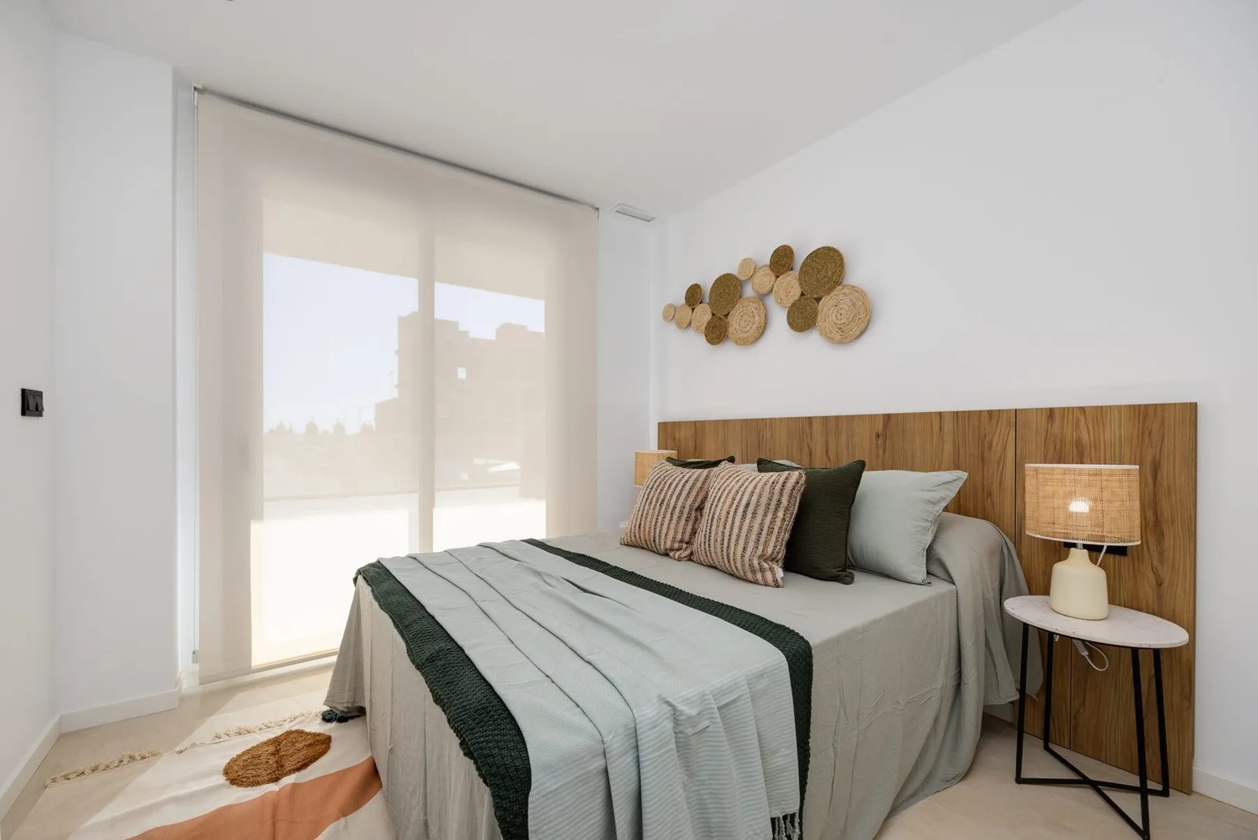 Photo of the show apartment’s main bedroom with a wooden headboard, a double bed and a large window with a blind