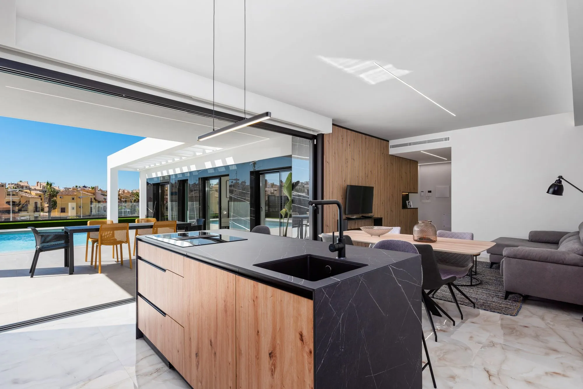 Kitchen island in wood and black marble effect with sink and hob, facing the open porch and pool