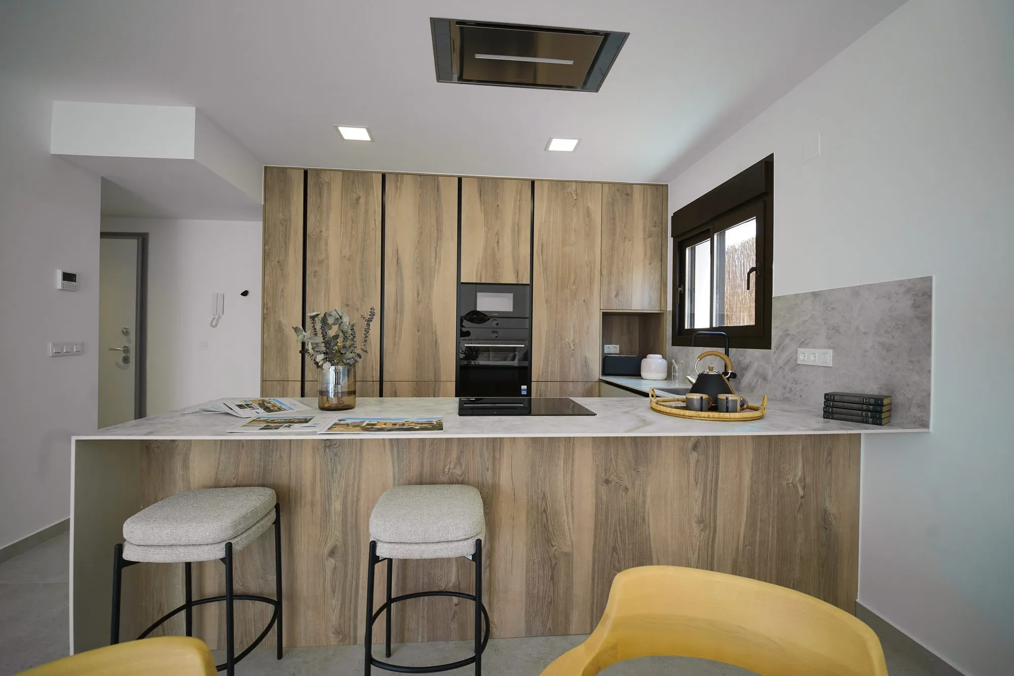Kitchen of the show home with wood-finish units, a peninsula with stools, built-in ovens and a ceiling extractor