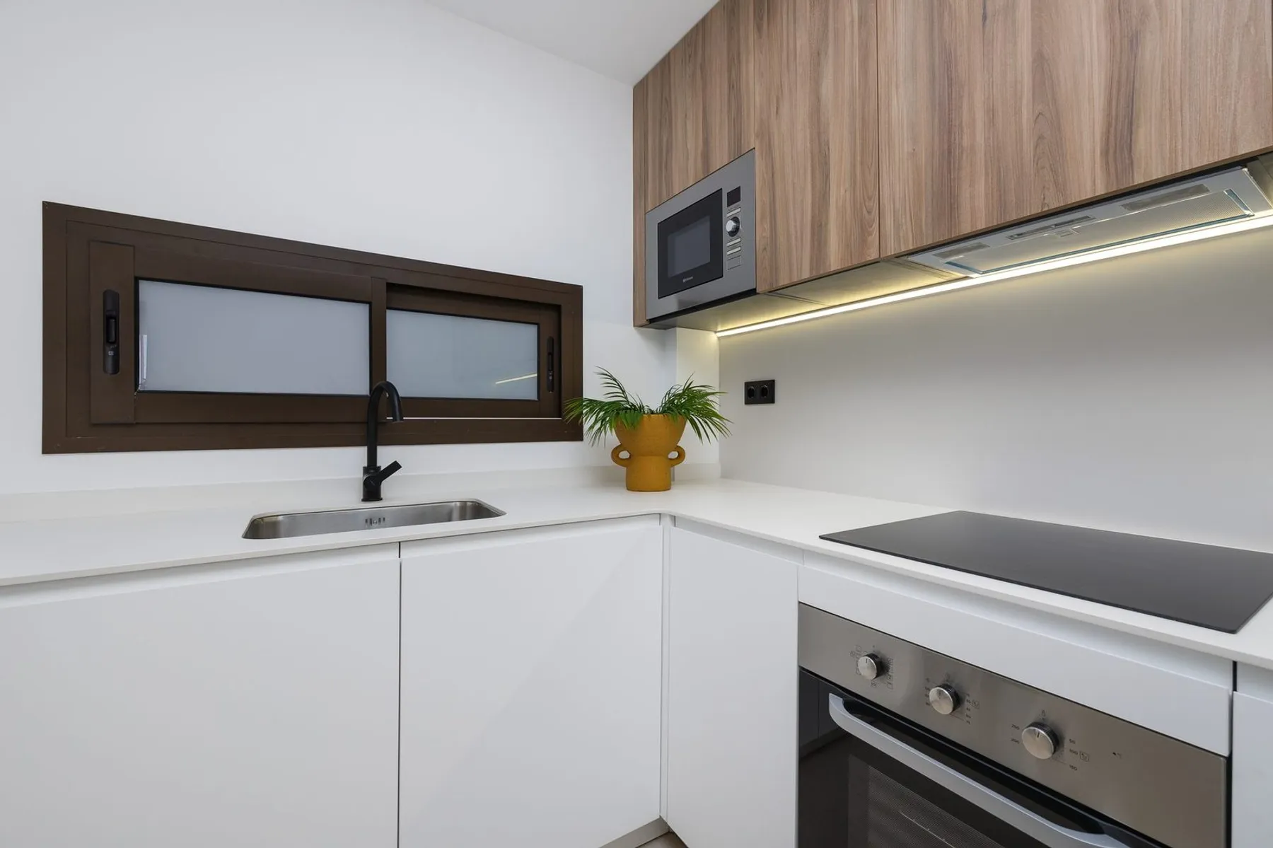 Photo of the show apartment’s U-shaped kitchen, white with wooden wall units, an induction hob, oven and microwave