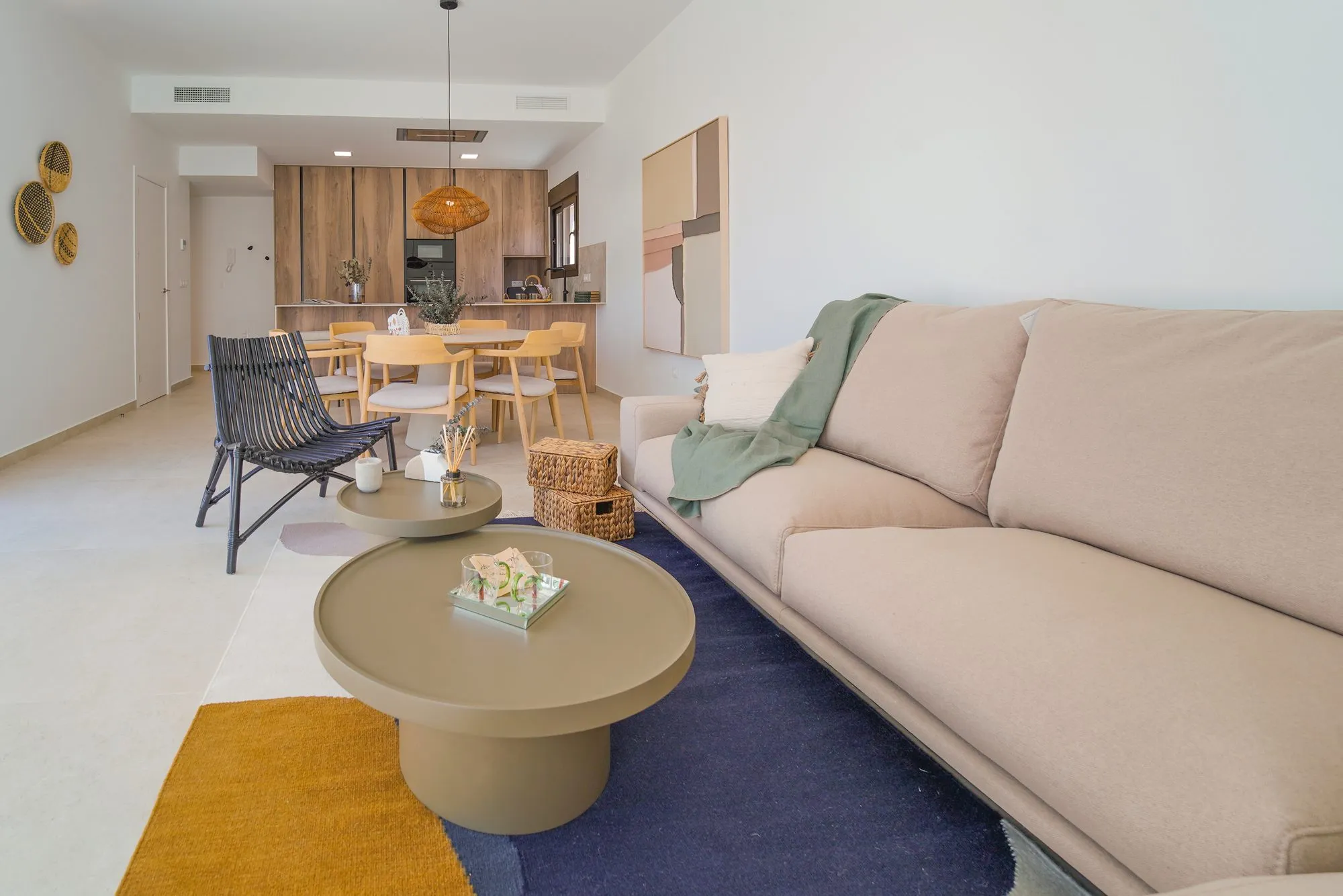 Living room of the show home with a sofa, coffee table and rug, and the dining area and kitchen beyond