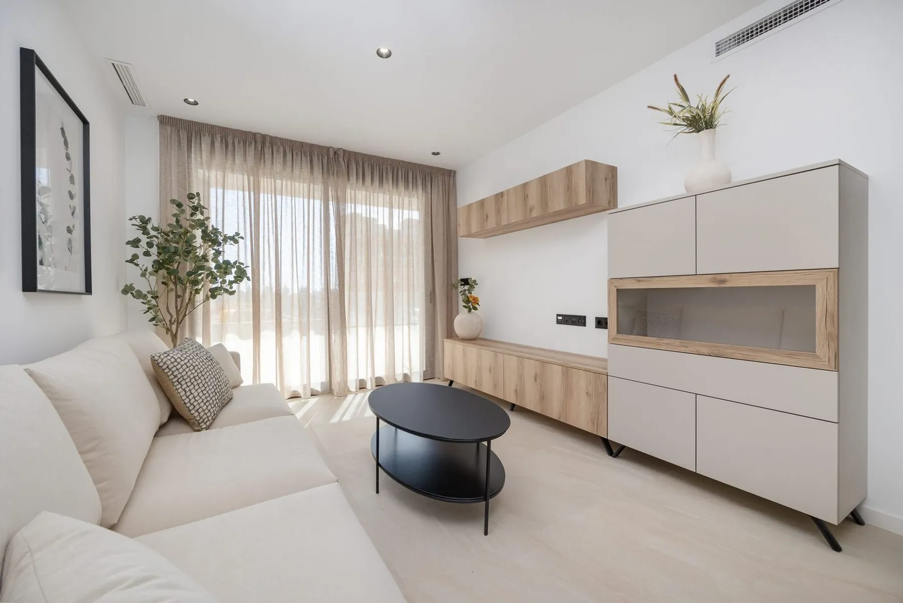 Photo of the show apartment’s living room with a pale sofa, a black coffee table, a wooden sideboard and floor-length curtains