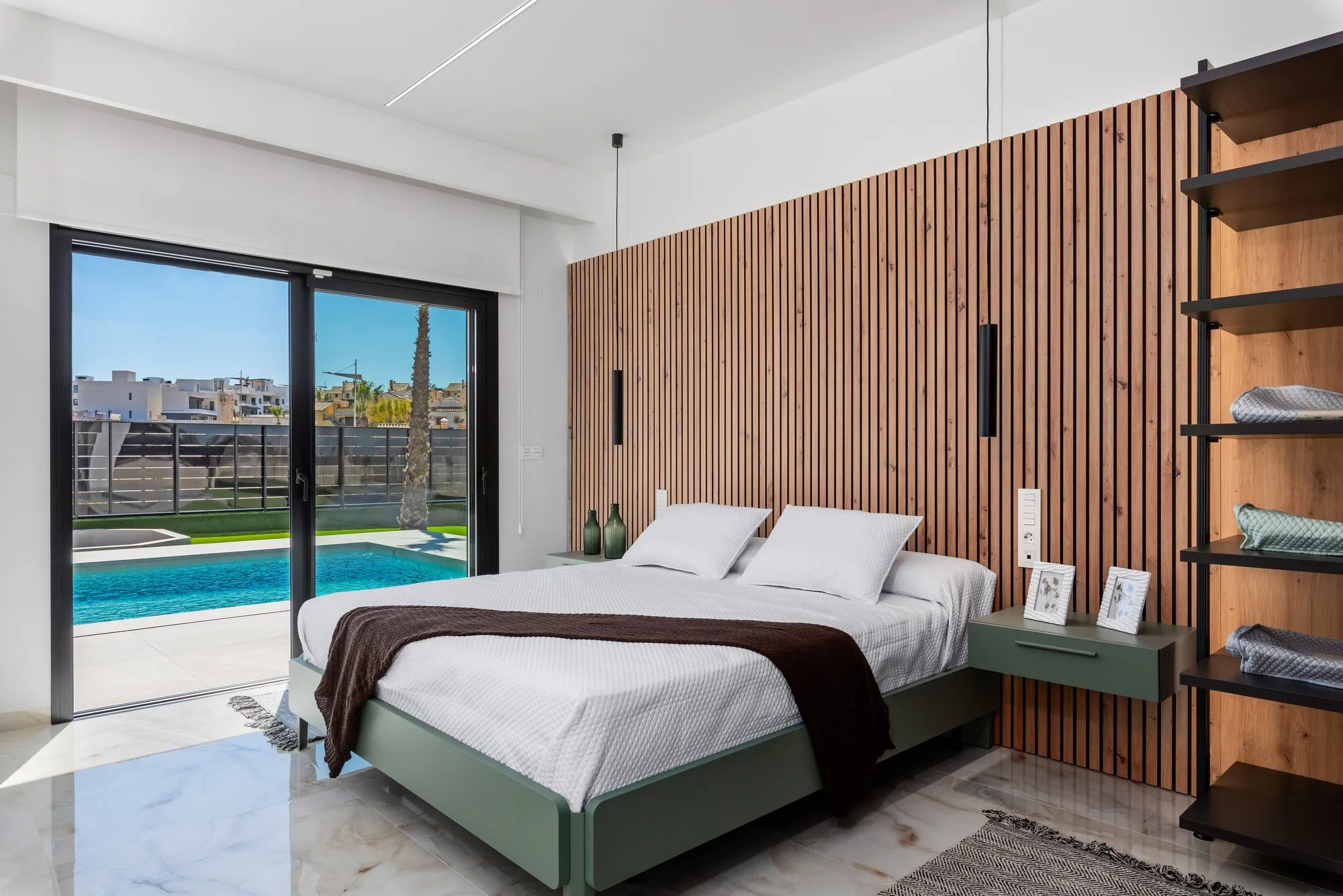 Main bedroom with a wooden slatted wall, a green-based bed and a sliding door out to the pool