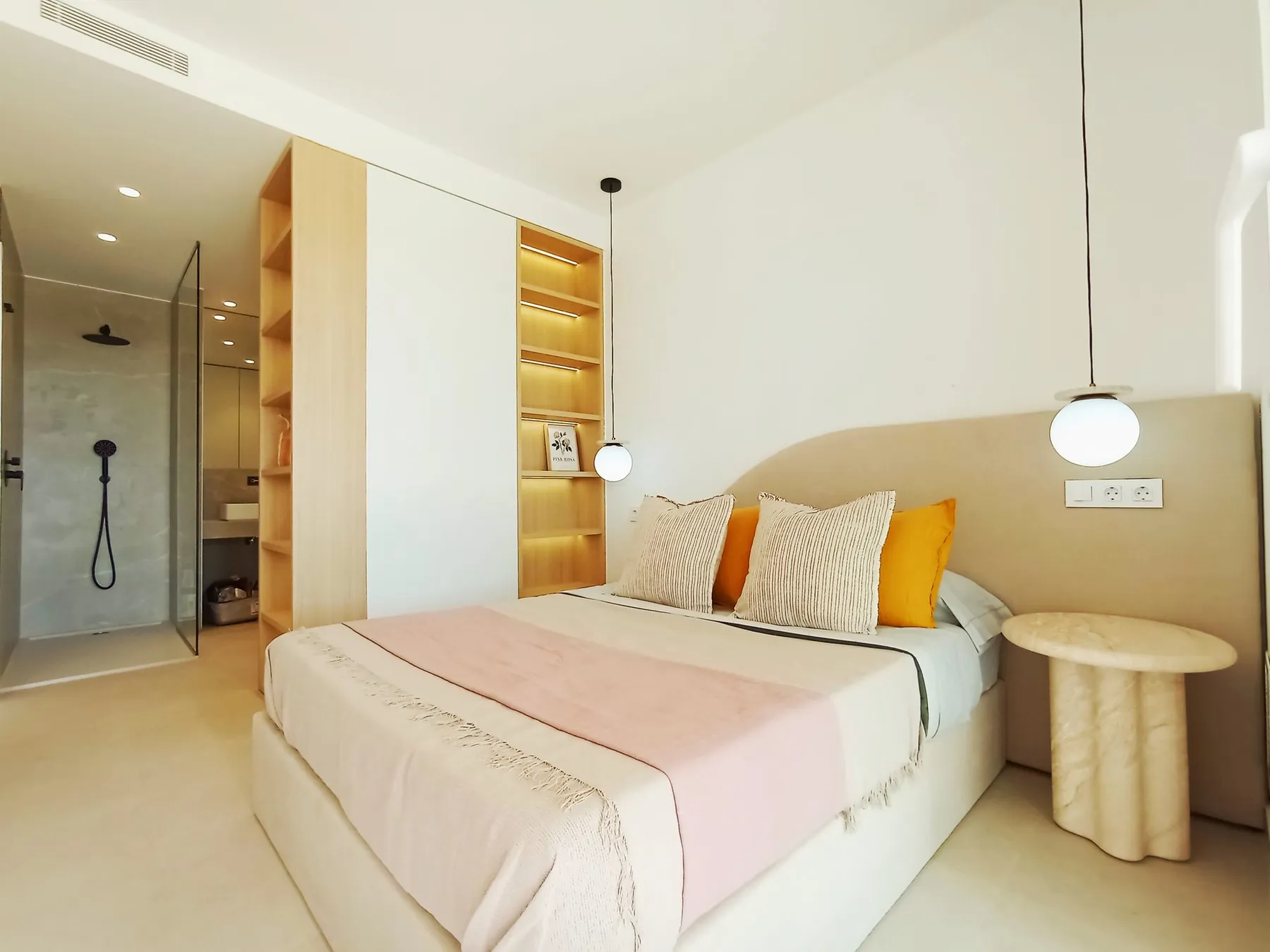Photo of the show flat main bedroom, a double bed with a curved headboard, lit wooden shelves and the en-suite shower behind a glass screen