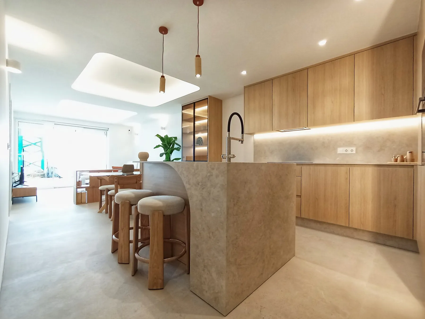 Photo of the show flat kitchen, wood-finish units, a stone-effect island with bar stools and a window onto the terrace
