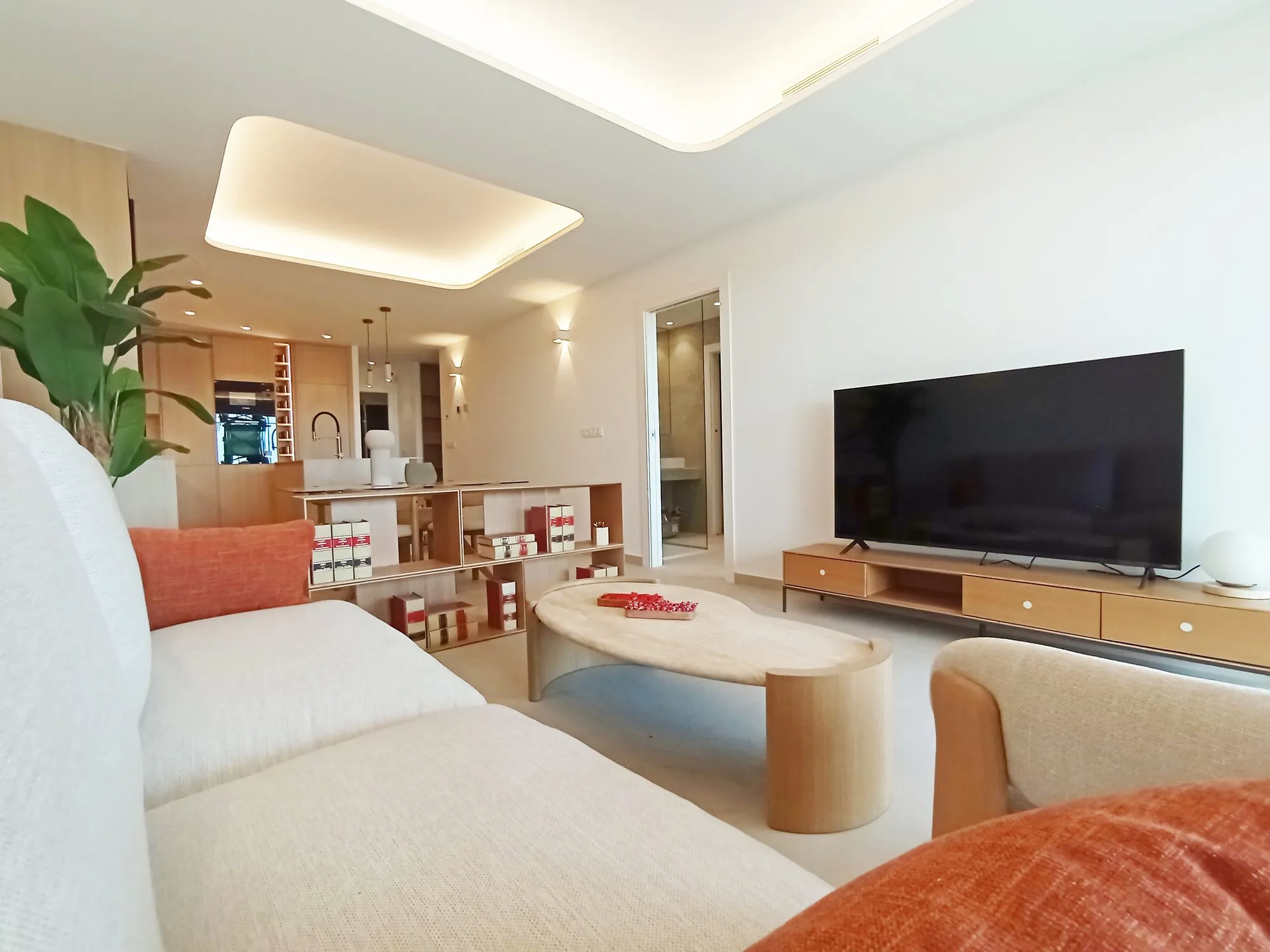 Photo of the show flat living room, a white sofa, a wooden coffee table and TV unit, and the kitchen at the far end