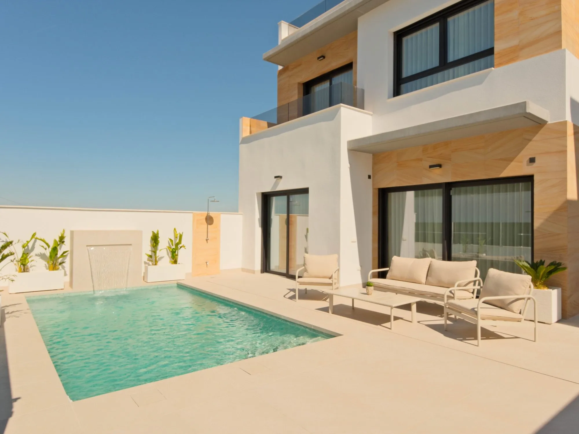 Photo of the show house, the private pool with a water feature, a terrace with outdoor furniture and the two-storey white and wood-effect façade