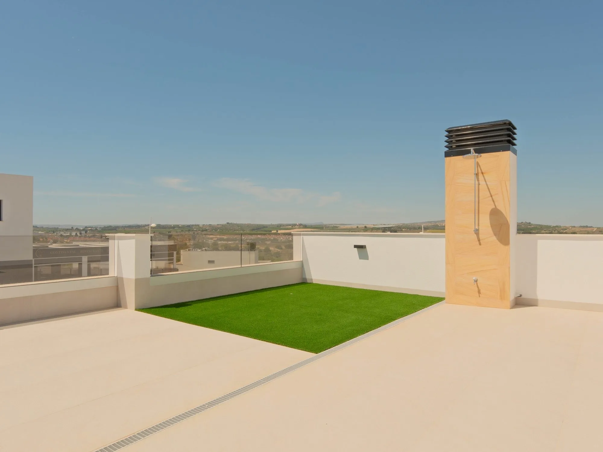 Photo of the show house solarium, a large tiled roof terrace with a patch of artificial grass and a glass railing