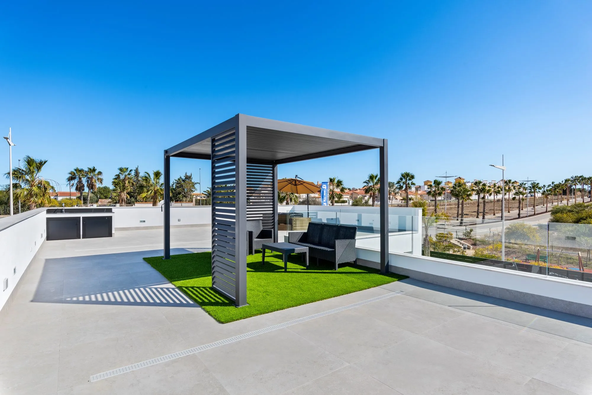 Rooftop solarium with a grey bioclimatic pergola over artificial grass, outdoor sofa and glass balustrade