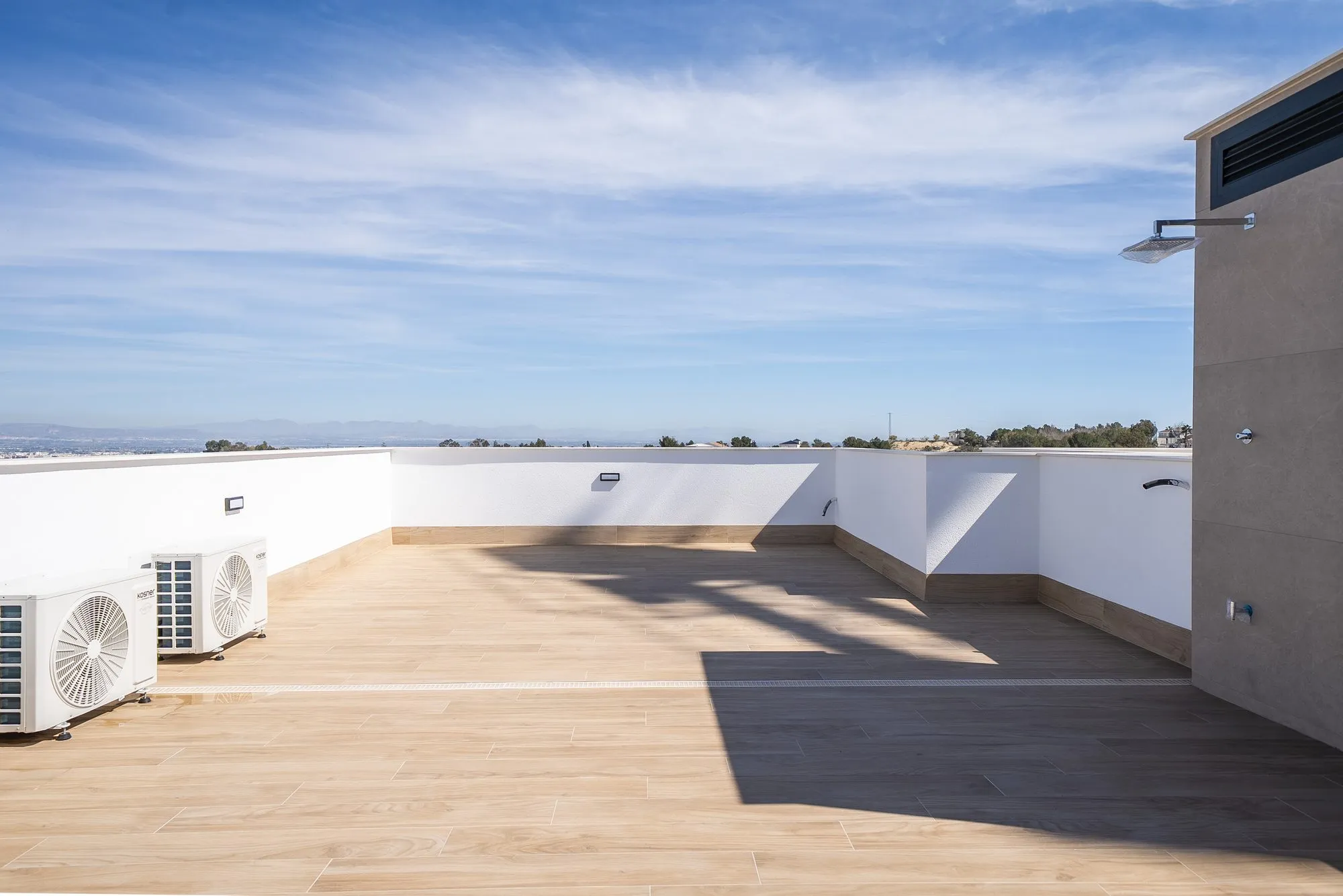 Rooftop solarium of an Arena Golf villa: wood-effect flooring, a white parapet, an outdoor shower and air-conditioning units