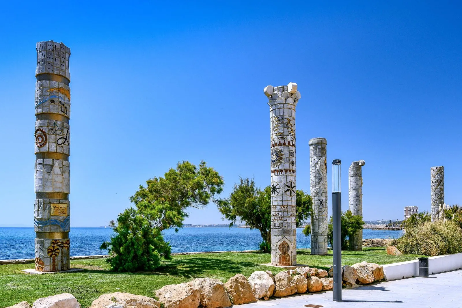 Carved stone columns on a lawn by the sea in Torrevieja, under a clear blue sky