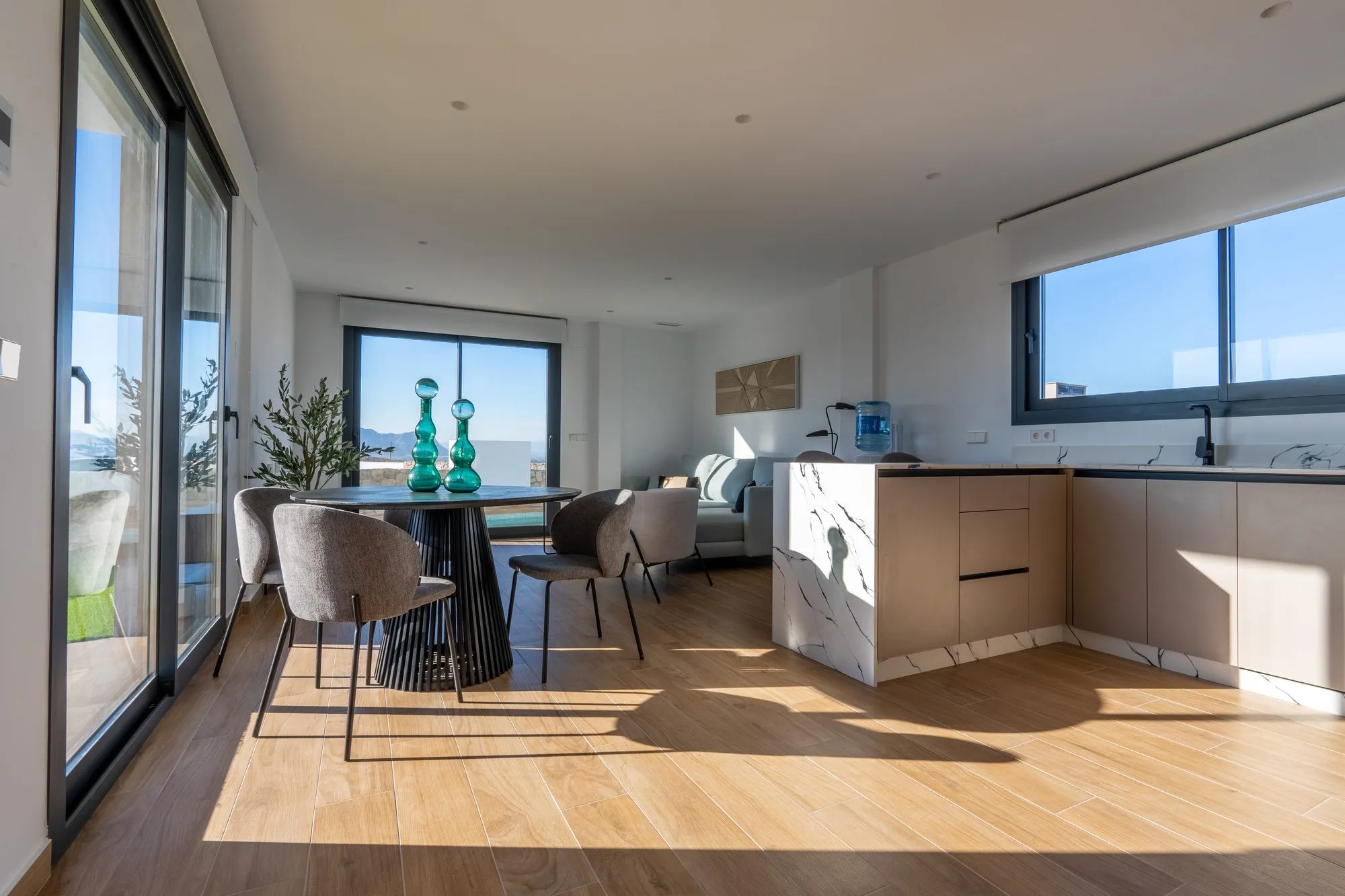 Dining area of show house 42: a round black table with grey chairs by the glass doors, the marble-effect kitchen island and the living room beyond