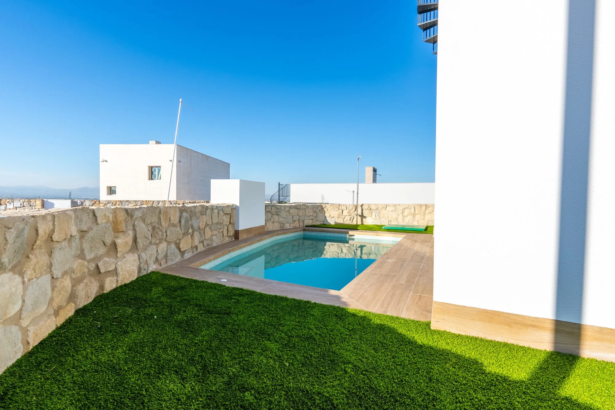 Garden of show house 42: a private pool with a wood-effect stoneware edge, artificial grass and a natural-stone wall