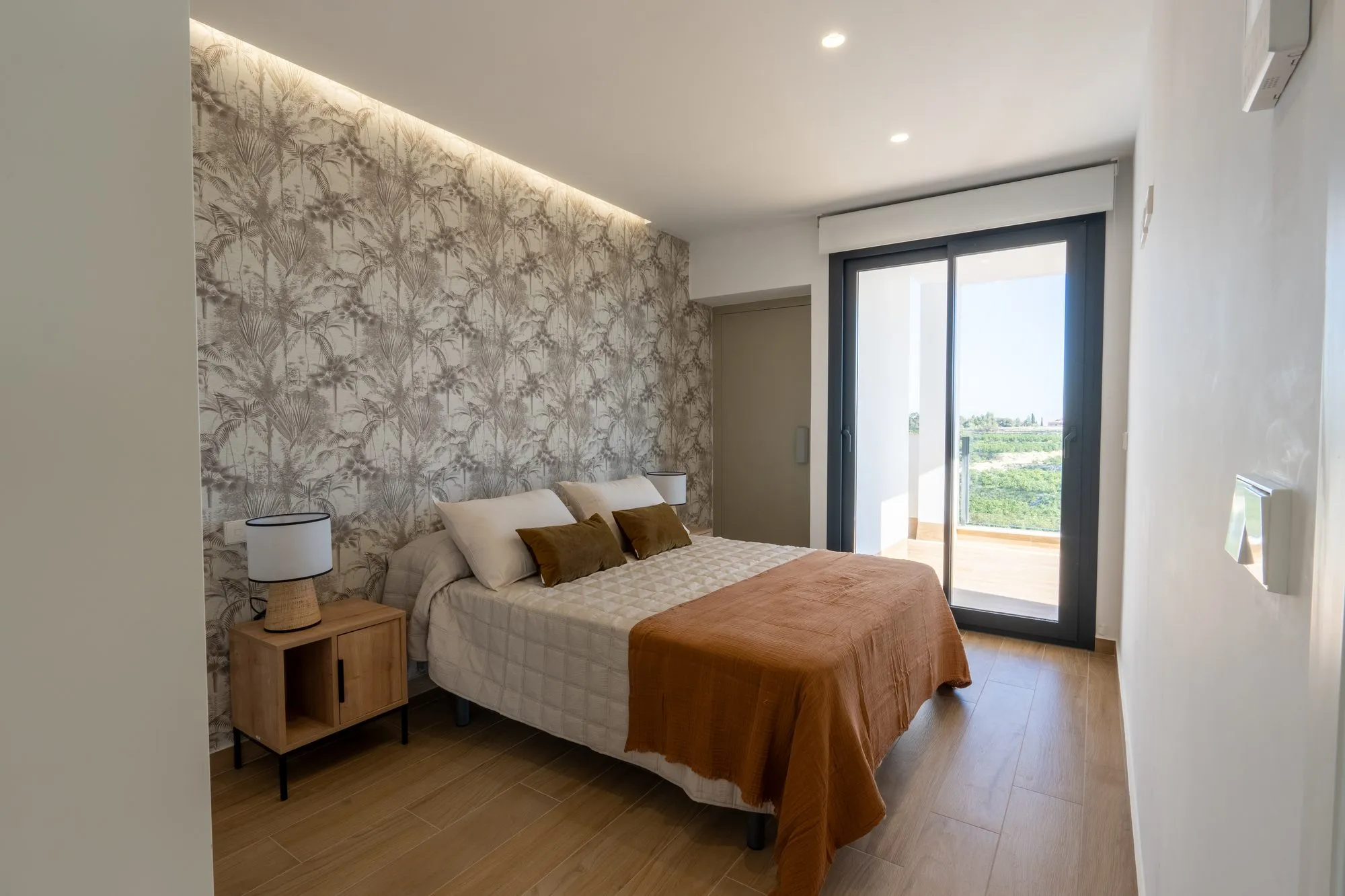 Main bedroom of show house 46 with botanical wallpaper, a double bed with a rust-coloured throw and a sliding door to the terrace