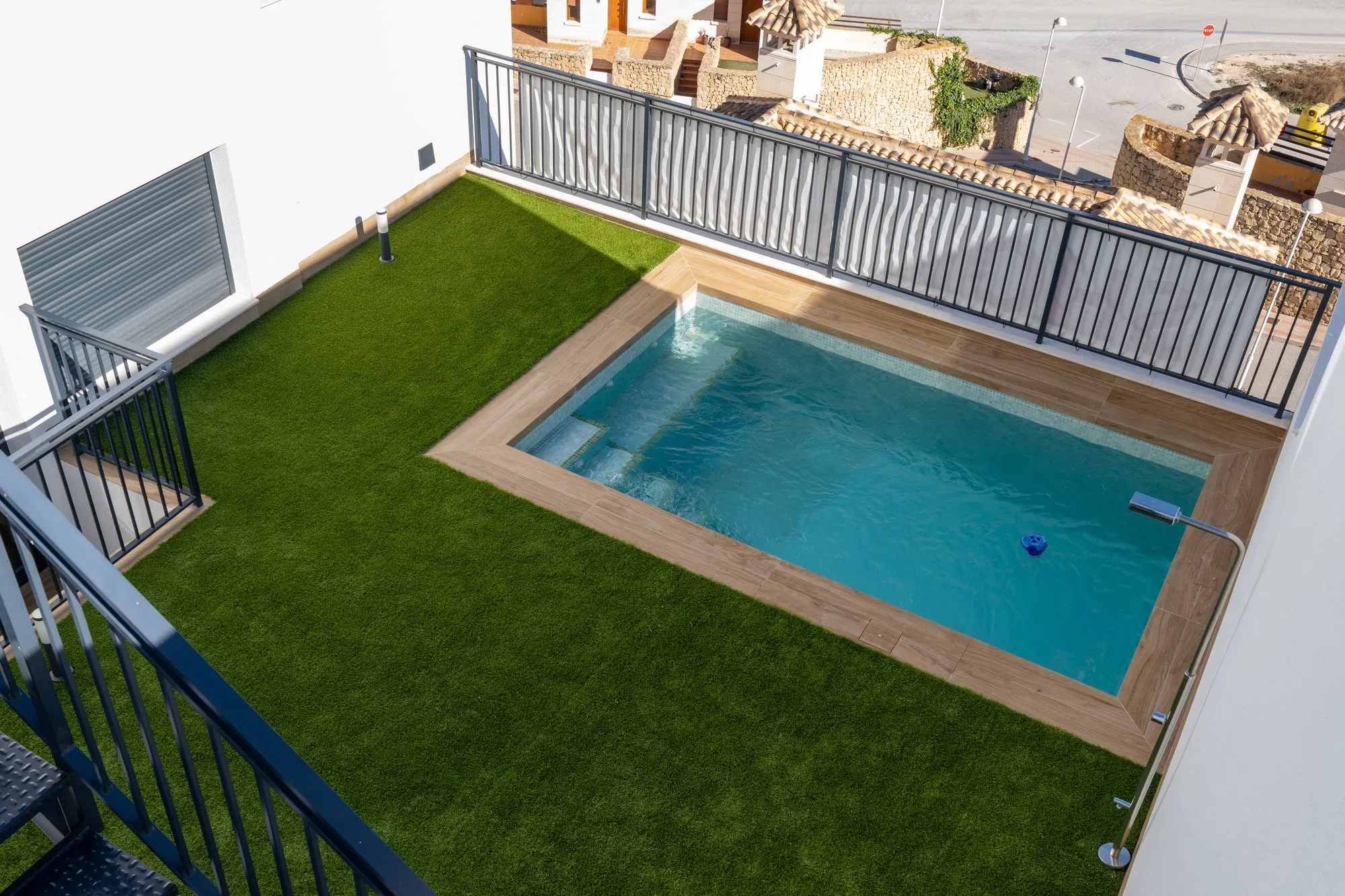 Garden of show house 46 seen from above: a rectangular pool with a wood-effect edge set in artificial grass, with black railings